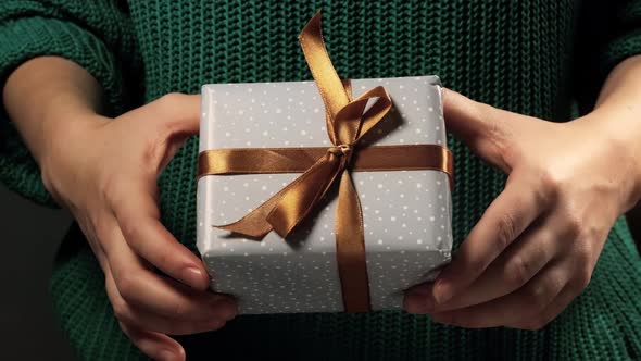 Girl  hand holding a gift wrapped in gray paper with white circles and tied with golden ribbon