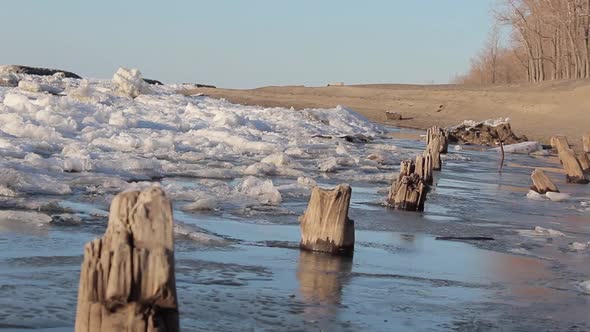 Dutch angle skewed tracking shot of a frozen lake, snow, ice, trees and pilings. alt