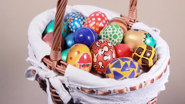 A Wicker Basket with Painted Eggs Swirls Against a Beige Light Background alt