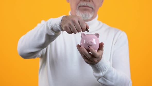 Senior Gentleman Putting Coin in Piggybank on Orange Background, Pension Fund alt