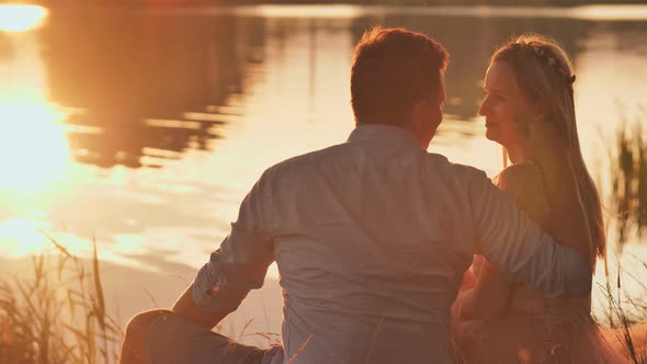 A Young Couple Sits on a Lake at Sunset