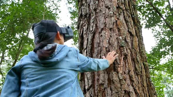 Happy woman wearing VR-headset glasses of virtual reality in forest and enjoying the nature. alt