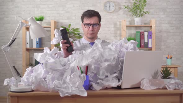 Unruffled Young Man Office Worker Is Talking on the Phone with a Heaps of Papers on the Office Desk alt