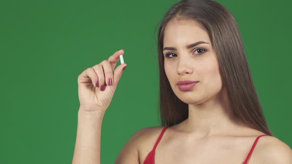 Gorgeous Woman Smiling Holding a Pill on Green Screen alt