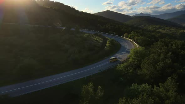 Aerial View of a Car Driving Along a Winding Mountain Road Through a Valley alt