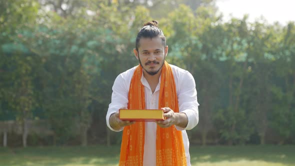 Indian man offering sweet box to the camera in an Indian traditional outfit Kurta Pajama alt