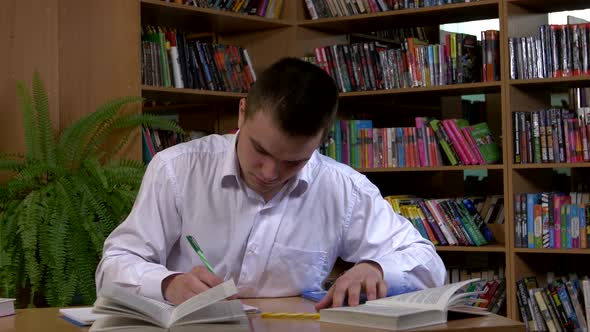 Male Student Researching with a Book in a Library alt