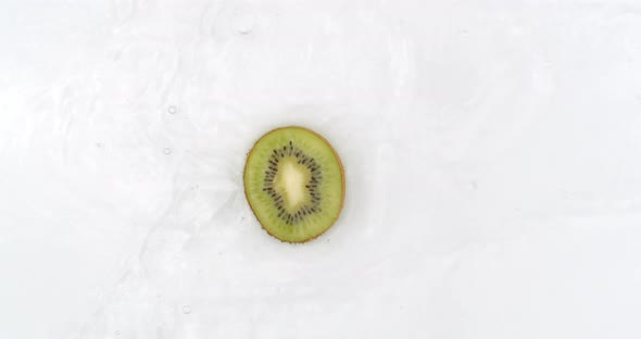 On a White Background, a Slice of Kiwi Falls Into the Water with a Splash alt