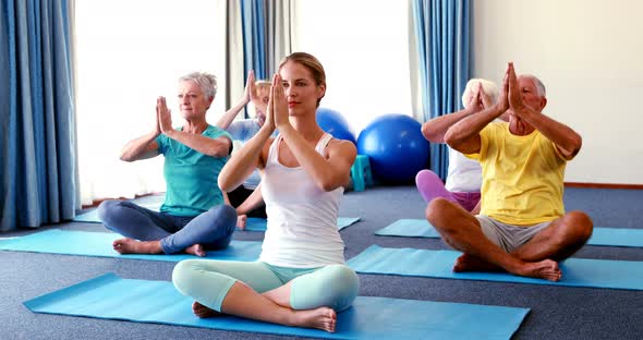 Trainer assisting senior citizens in practicing yoga alt