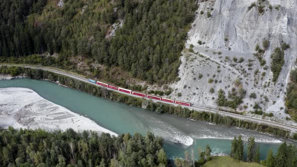 Red train drives in the scenic rhine canyon in Switzerland, aerial view. alt