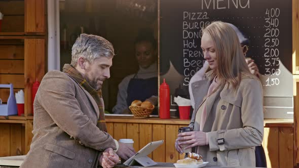 Young woman bringing coffee to man by food booth