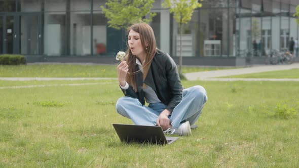 Young Stylishly Dressed Girl Sitting in the Park on the Grass Near the Computer alt