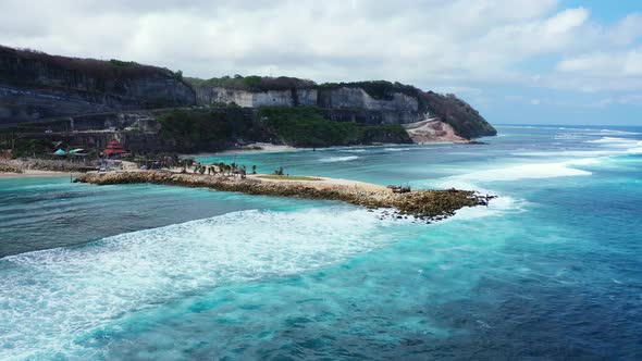 Beautiful sea scenery with white waves splashing on rocky pier seaside, slopes of green hills in Bal alt