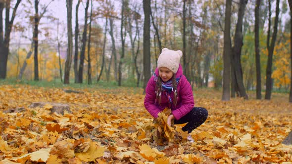 Excited Girl Throwing Fallen Autumn Foliage in Park alt