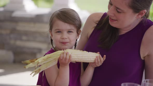 Young girl eating corn at backyard barbeque