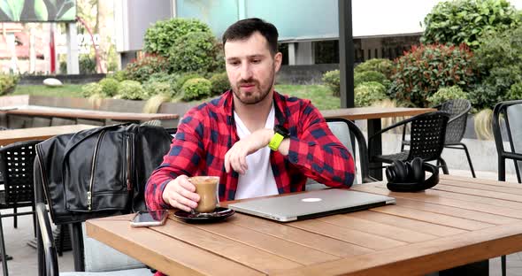Bearded young man working at computer while having cup of coffee.