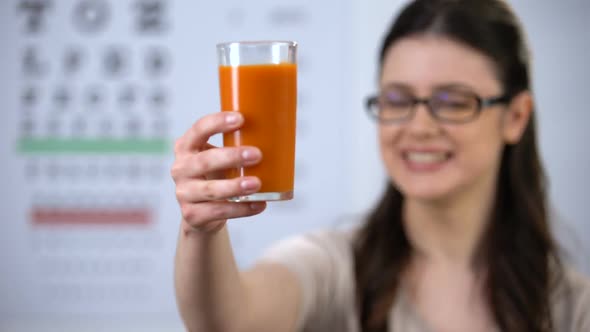 Woman in Spectacles Showing Glass With Carrot Juice, Beta Carotene, Vitamins alt