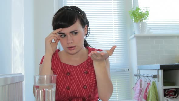 Female taking headache tablet in kitchen