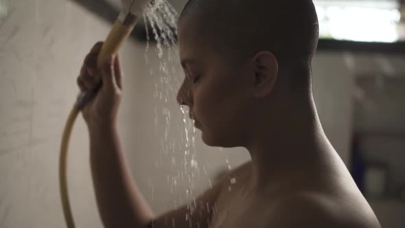 Sick and weak bald Asian girl is bathing with hand shower in bathroom is very sad and crying due to alt