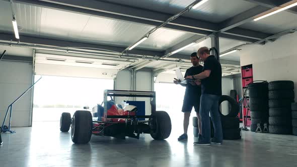 Two Specialists with a Laptop are Talking Next to the Racing Cart alt