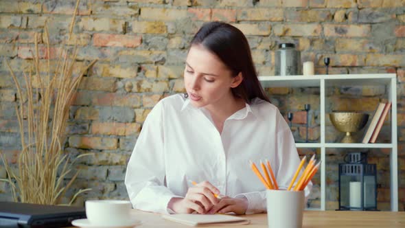Young Beautiful Woman Making Notes at Tha Table and Talking on the Phone alt