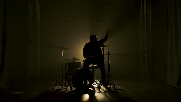 Silhouette Drummer Playing on Drum Kit on Stage in a Dark Studio with Smoke and Neon Lighting alt