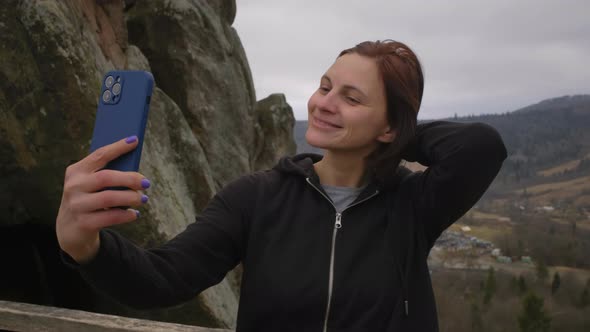 30s White Female Tourist Making Selfie Photo on Mobile Phone Standing in Mountains alt
