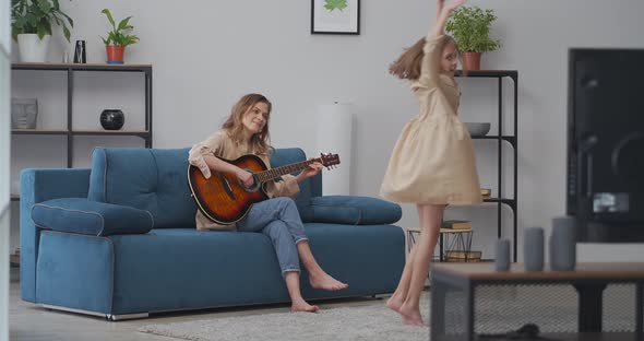 Funny Little Girl is Dancing When Her Mother is Playing Guitar at Home Happy Childhood and Parenting alt