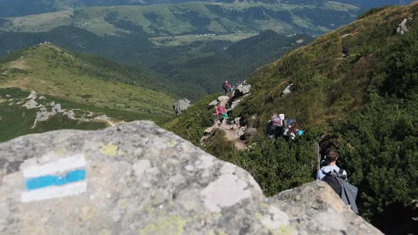 Group of Tourists and Children with Backpacks Go Down on Stone Trail in Mountain alt