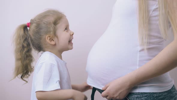 Funny Girl Kisses Large Tummy of Pregnant Mommy at Wall alt