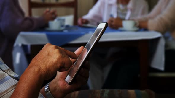 Senior man using digital tablet with his friends sitting in background 4k alt