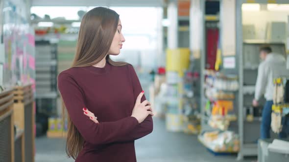 Bored Young Beautiful Caucasian Woman Looking Back at Absorbed Man Choosing Supplies in Hardware alt