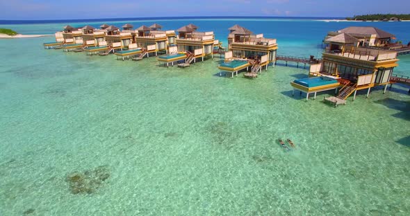Aerial drone view of a man and woman couple with seascooters snorkeling near overwater bungalows. alt
