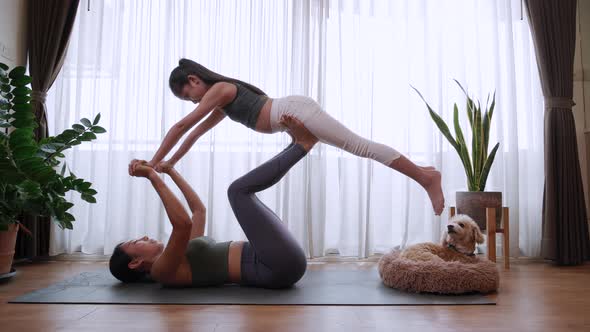 Healthy mom lifts up little girl like flying in a yoga pose in living room at home, Happy family