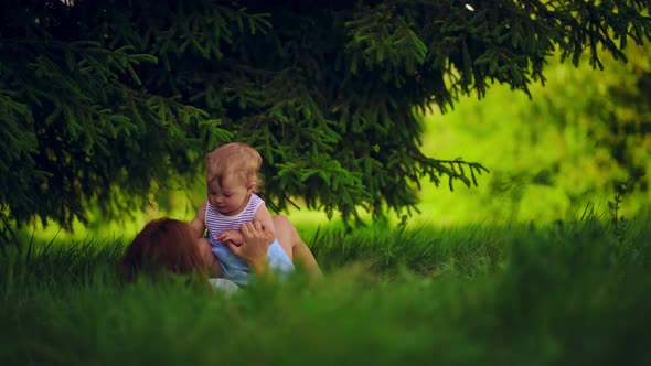 Mom with a child have fun lying in a park under a tree. alt
