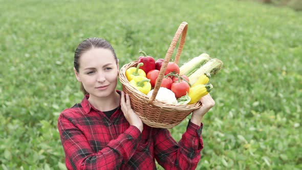 A farmer woman carries a basket of vegetables through an agricultural field. Agribusiness concept. alt