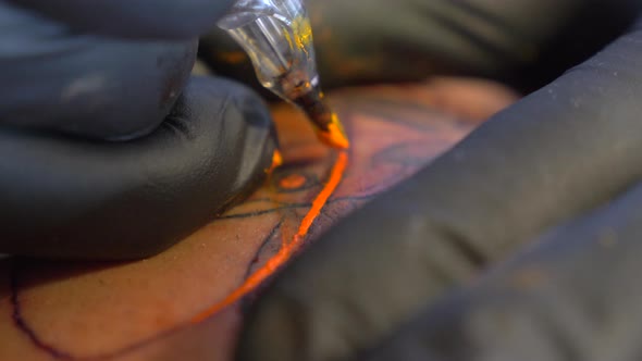 A Tattoo Artist Carefully Putting The Orange Color On His Tattoo Art Design While Wearing His Black alt