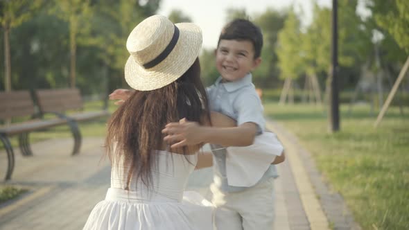 Back View Elegant Middle Eastern Mother Sitting Park Alley As Son Running Hugging Parent alt