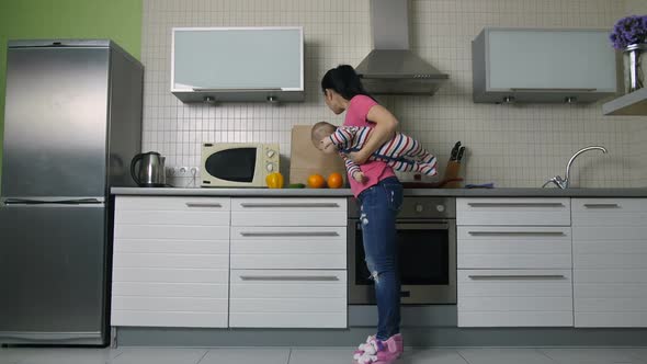 Mother with Baby Unloading Shopping Bag in Kitchen alt