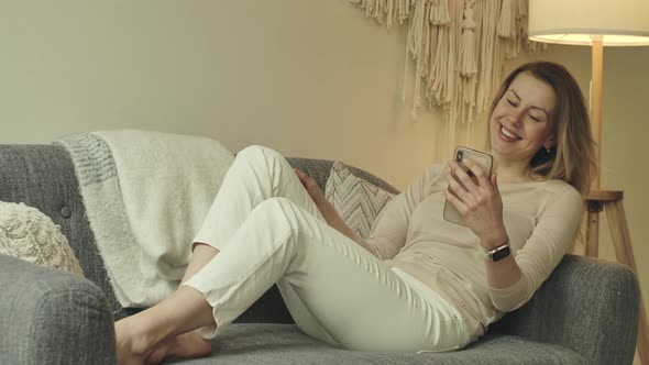 Bare Feet Girl Sits on Couch with Smartphone in Hands