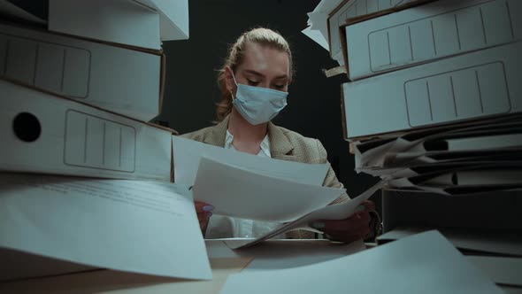 Tired Businesswoman Wearing Medical Protective Mask with Pile of Folders Working in Office Female alt