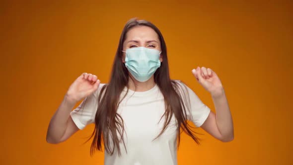 Woman in Medical Mask on Face is Very Happy and Claps Her Hands Against Yellow Background alt
