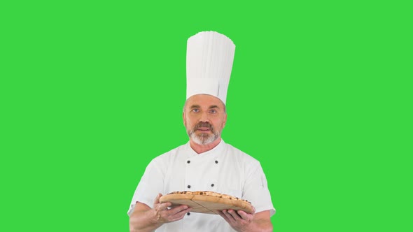 Attractive Cook with a Pizza in Hands Walking and Talking To Camera on a Green Screen, Chroma Key. alt