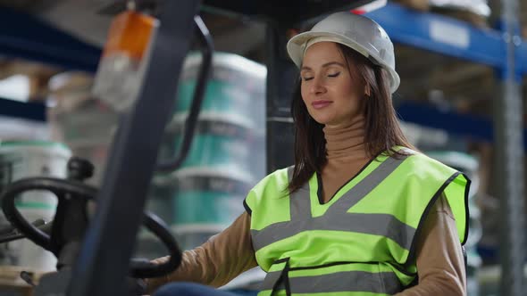 Charming Coquette Caucasian Woman in Hard Hat Sitting in Warehouse Autoloader Turning Looking at alt