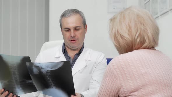Mature Male Doctor Examining X-ray Scans of a Senior Female Patient