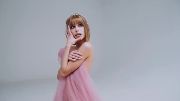 Attractive young Caucasian woman with a Bob haircut in a pink dress on a white background