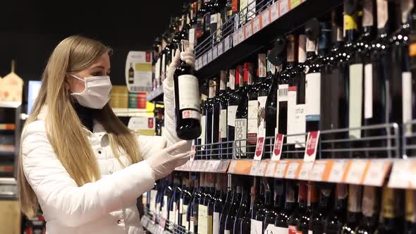Ukraine, Ternopil, April 24, 2020. Blonde in a protective mask, choosing wine in the supermarket. alt