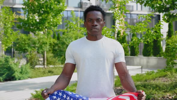 Serious Afroamerican Man Holding an American Flag Looks Camera and Says USA alt