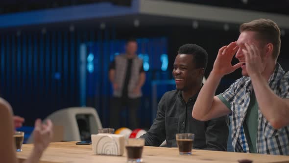 A Joyful Man Runs Up to Friends Giving Five Different Ethnic Groups of People Sitting at a Table in alt