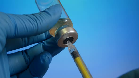 The Hands of a Doctor in Blue Gloves Draw the Vaccine From a Vial Into a Syringe